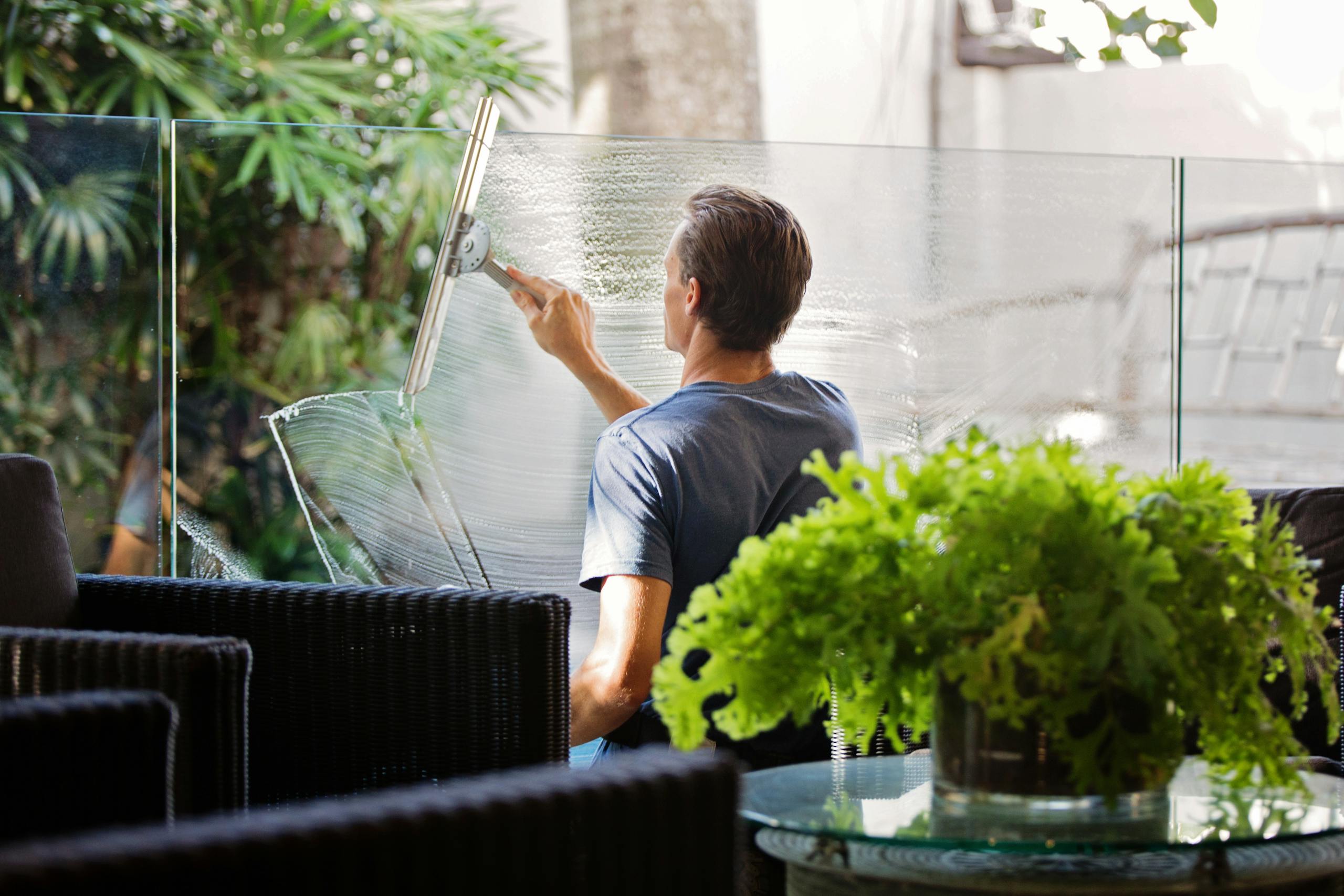 Man in Gray Shirt Cleaning Clear Glass Wall Near Sofa